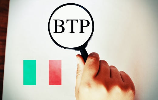 Hand holding a magnifier with the text BTP translating as Italian government bonds.