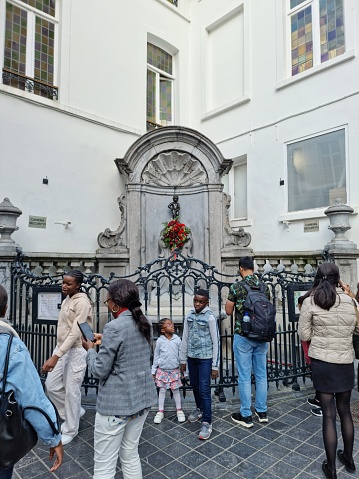 Manneken Pis is a landmark 55.5 cm  bronze fountain sculpture in central Brussels, Belgium. The image shows the fountain with several people arround it.