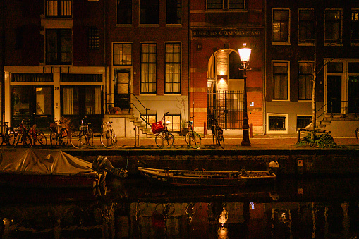 In Amsterdam, Netherlands city lights illuminate the canal at night.