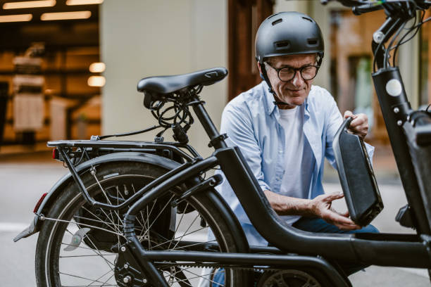 homme âgé changeant la batterie sur un vélo électrique - electric bicycle photos et images de collection