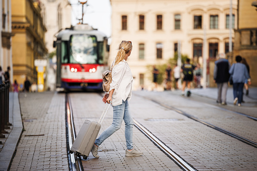 Travel carefully and safety with insurance and avoid accidents. Woman tourist with suitcase walks across city street while tram arrives
