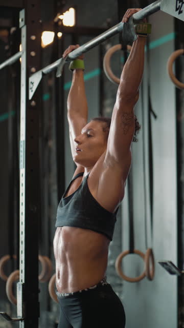 Vertical shot of a focused woman  doing pull-ups on the bar, training at a gym