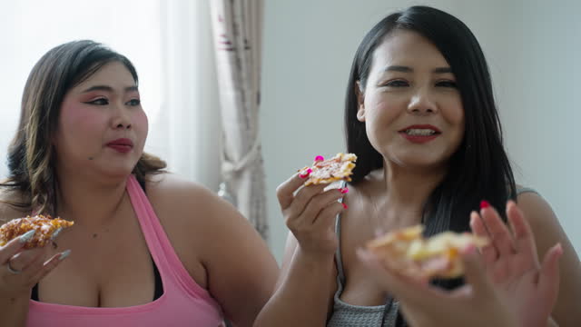 Group of Asian overweight woman friends enjoy eating pizza together in living room at home.Junk food, Fast food, Unhealthy food concept