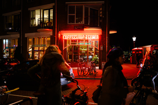 In Amsterdam, Netherlands people are silhouetted by the red lights illuminating a coffe shop at night.