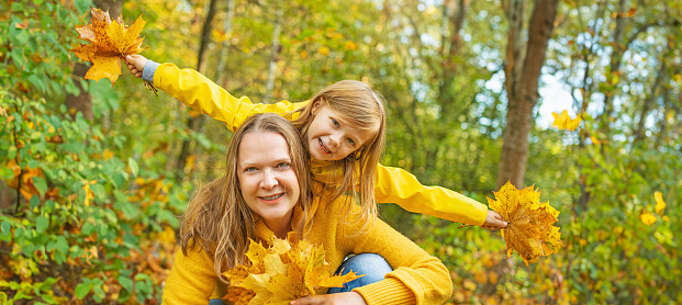 Little girl and mother with autumn leaves as a bouquet in the yellow autumn park.