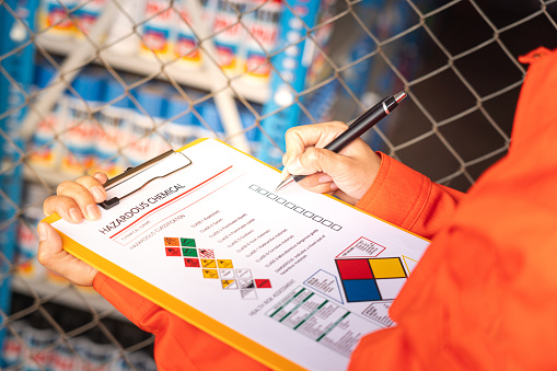 A worker is checking on the hazardous chemical material information form with background of chemical storage area at the factory place. Industrial safety working action. Selective focus.