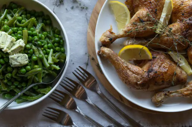Homemade baked chicken legs with green beans and green peas on a dinner table. Healthy low carb meal