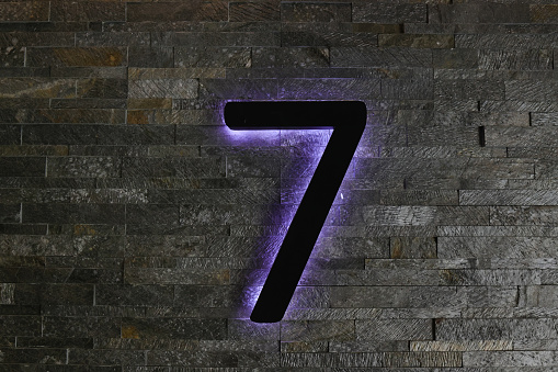 Dark  Neon Font with fluorescent purple tubes Number 7 on the dark brown brick wall.  Night Show Alphabet.