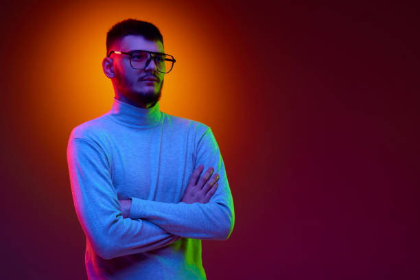 istock Handsome young bearded man dressed casually in glasses crossed his hands and think against gradient background in mixed color light, filter. 1688705355