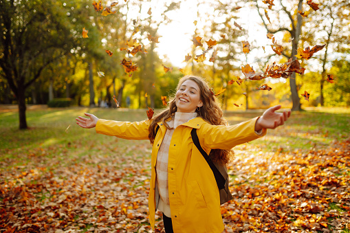 Beautiful woman throwing autumn yellow leaves. Happy female tourist having fun and enjoying nature in autumn park. The concept of relaxation, fun, solitude with nature.