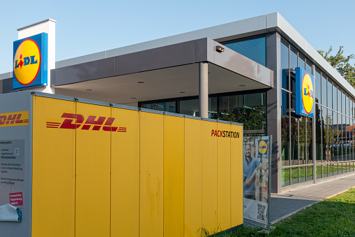 Amberg, Germany - September 10, 2023: Packstation - Parcel locker of DHL Germany, it belongs to the Deutsche Post. DHL was founded in San Francisco and has now its headquarter in Bonn, Germany. In the background a store of the LIDL supermarket chain in the german town Amberg. LIDL has its headquarter in Neckarsulm, Germany with over 10000 stores in Europe.