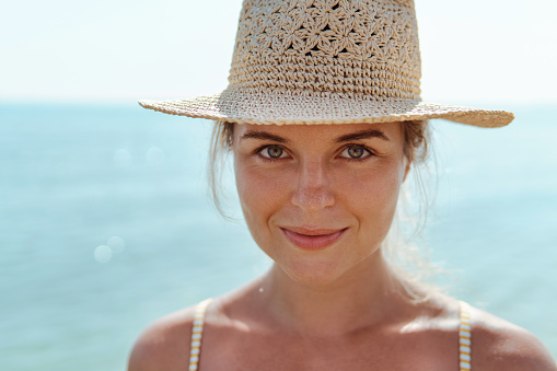 Woman radiates summer vibes wearing yellow striped bikini and a straw hat, enjoying her time on the beach.