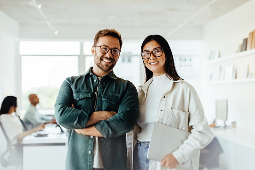 Portrait of two business people standing together in an office. Happy business professionals working as a team in a creative workplace.