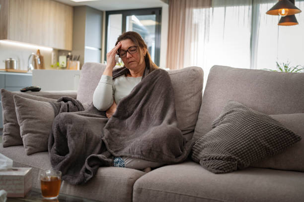 istock Sick woman with flu and headache eyes closed and touching her head on sofa 1688746656