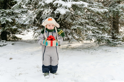 Cute little boy holding a Christmas gift in the snow forest