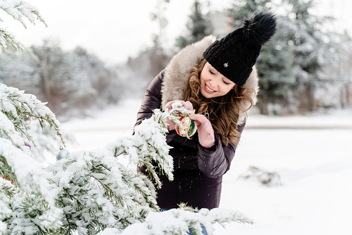 Happy woman decorating snow covered Christmas tree outdoors