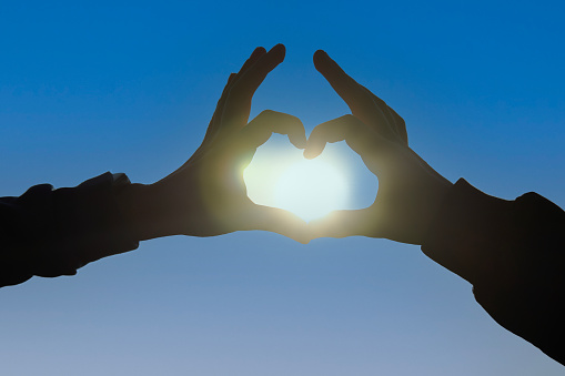 Silhouette of hands making heart with sun inside, close-up. Heart shape making of hands against beautiful sunset. Love and Valentines day concept