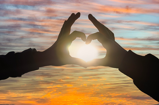 Silhouette of hands making heart with sun inside, close-up. Heart shape making of hands against beautiful sunset. Love and Valentines day concept
