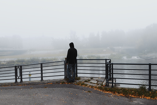 Young man standing in front of railing and looking to river Vltava in city Ceske Budejovice with fog