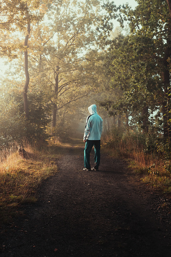 Young man in white hoodie and pants standing through misty fog forest from side