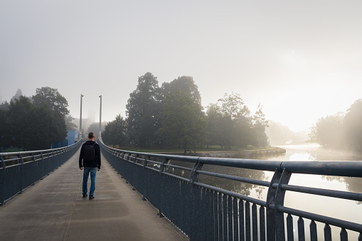 Young man walking on bridge over river Vltava in city Ceske Budejovice with fog