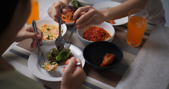 Aerial view of young asian woman serving vegetable salad onto a friend's plate between have dinner together at home