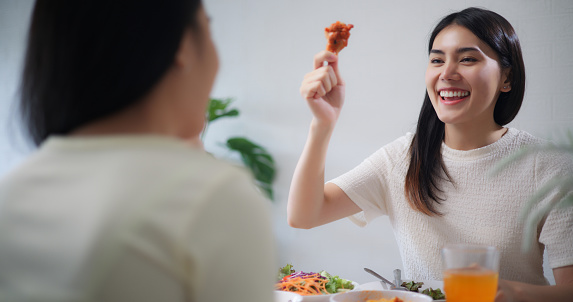 Joyful young asian woman and girl friends cheers with fried chicken and drink during having celebrating holiday together at home, Teenager eating and drinking concept