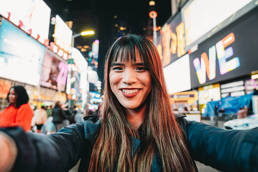 Pov view of an asian woman taking a selfie in Times Square, New York City. Many advertising billboards in the background.