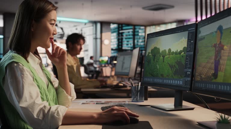 Creative Asian Woman Using Desktop Computer And Designing In 3D modelling Software Unique World And Characters For RPG Video Game In Diverse Office. Female Game Designer Creating Immersive Gameplay.