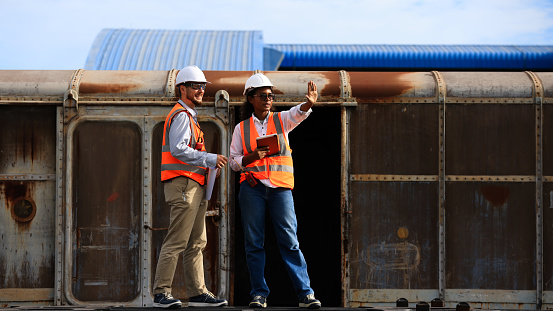A couple of logistic engineers with safety vests working at the container yard at the train shipping area