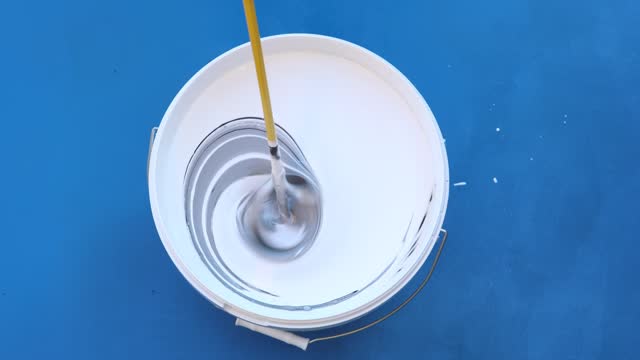 Paint mixer is placed in wall paint bucket to mix and stir three paint colors.