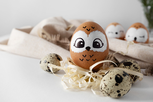Funny owl. Brown Easter eggs, quail eggs on yellow straw. Light background.