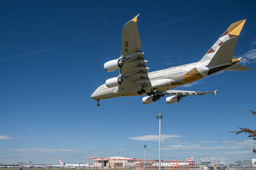 Etihad Airways Airbus A380-861 approaching to land at Heathrow Airport in London, with airport buildings in the background