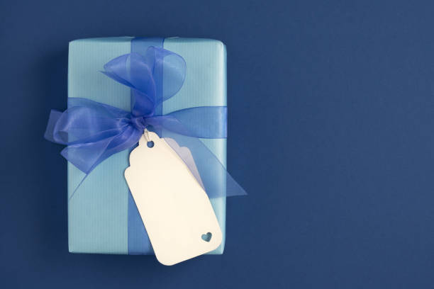 istock Blue gift box with blue bow and white gift tag. Blue background, space for text. Card for the holiday. 1688826664