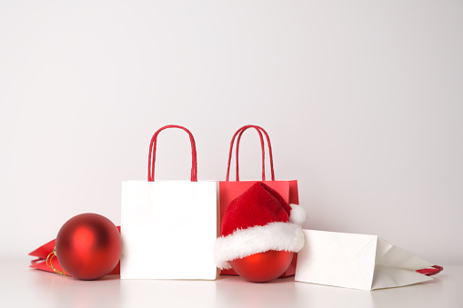 Christmas sales and shopping concept. Paper bags with red ornament in santa hat.