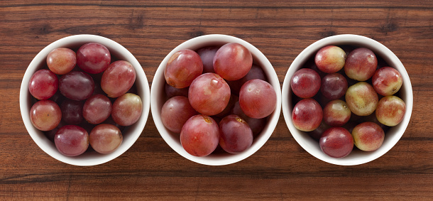 Three bowls containing different types of red grapes