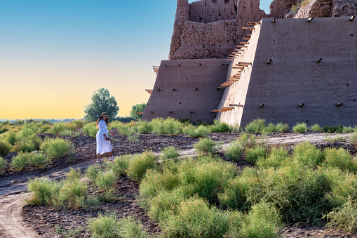 Lady wearing a white dress and a hat is exploring the Khorezm fortress, Uzbekistan