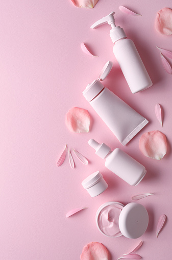 Different pink cosmetic  products with flower petals and copy space