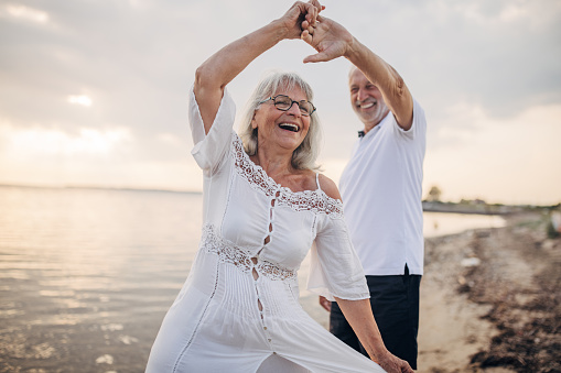 Man and woman, happy senior couple dancing on the beach by the sea together.