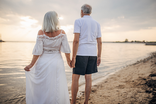 Man and woman, senior couple standing on the beach by the sea together.
