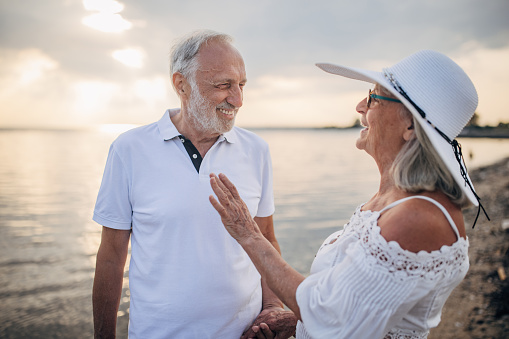 Man and woman, happy senior couple standing on the beach by the sea together.