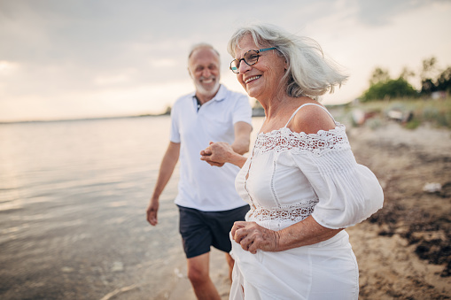 Man and woman, happy senior couple taking a walk on the beach by the sea together.