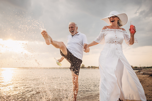 Man and woman, happy senior couple having fun on the beach by the sea together.