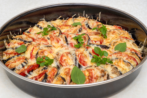 Eggplants with tomatoes baked with cheese and garlic sauce and sprinkled with basil leaves. Home cooking.