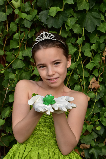 a sweet GIRL PLAYING  in a garden to be  a PRINCESS AND her pince is a PLASTIC Frog