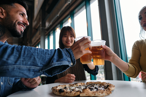 Group of friends enjoying and toasting with beer before eating their delicious pizza