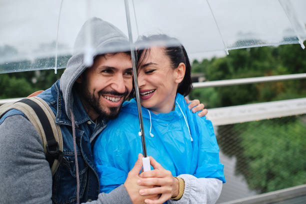 Happy young couple standing under an umbrella and looking around the city.