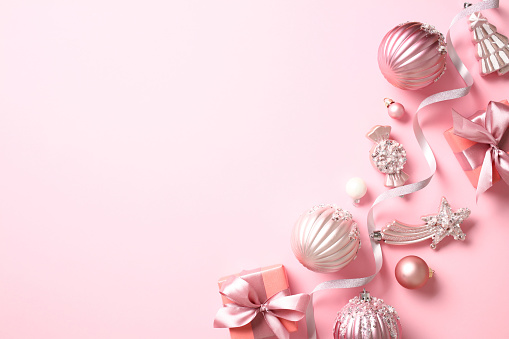 Christmas banner design. Top view photo of stylish Christmas decorations, ribbon, balls, gift boxes on pink background.