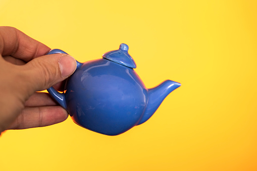 a small blue ceramic teapot for making tea in your hand on a yellow background. Minimalist Ceramic Teapot