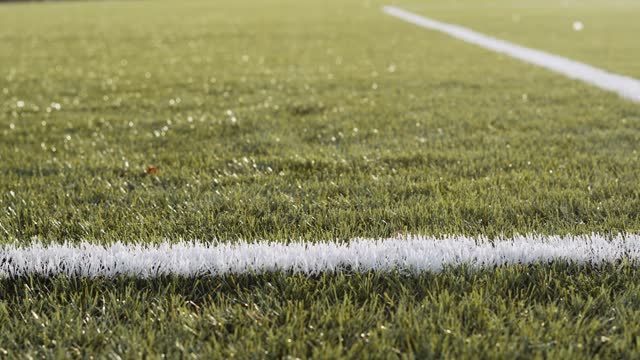 Old soccer ball jumps behind white lines on football pitch.